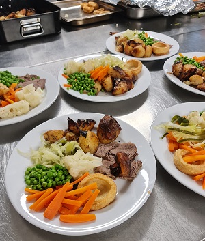 several plates with potatoes, veggies, and roast on a stainless steel counter